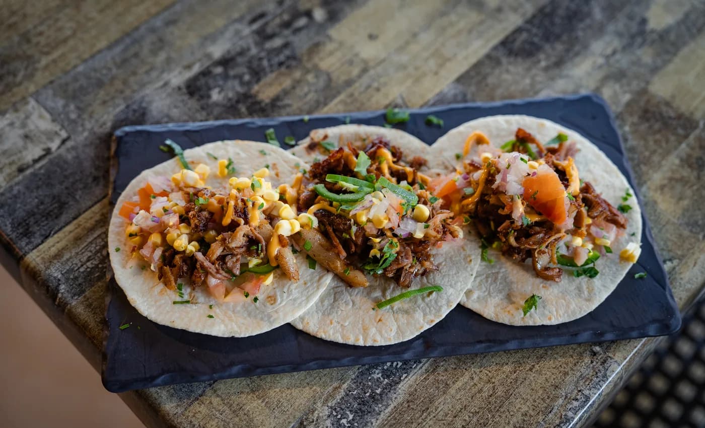 Three freshly dressed tacos served on a slate board at The Old Forge